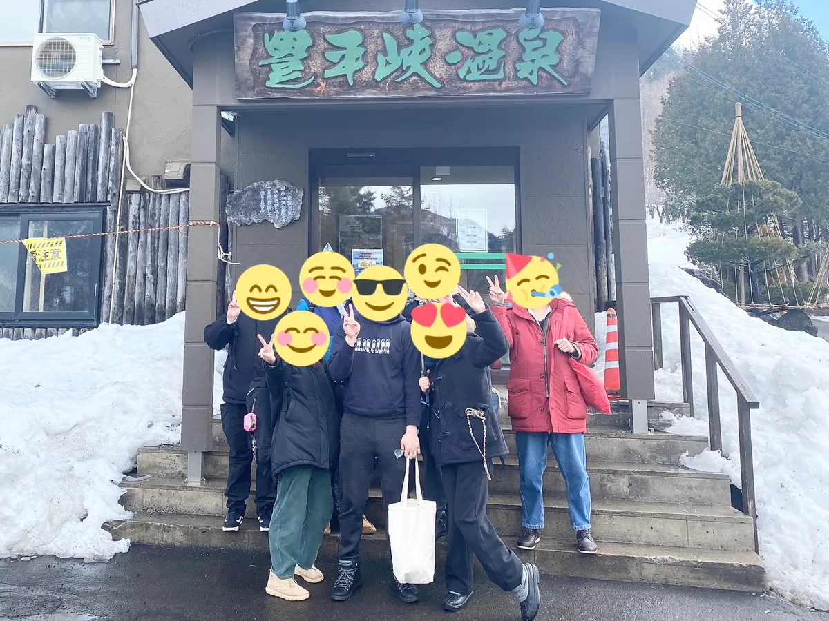 雪の残る温泉施設の前で記念撮影する様子